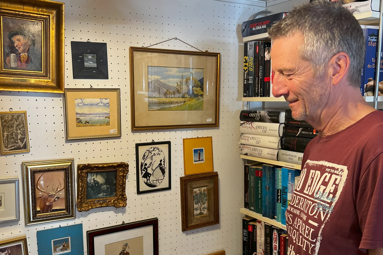 Ein Freiwilliger steht im Innern eines Brockenhauses vor einer Wand mit etlichen Büchern und Bilderrahmen.